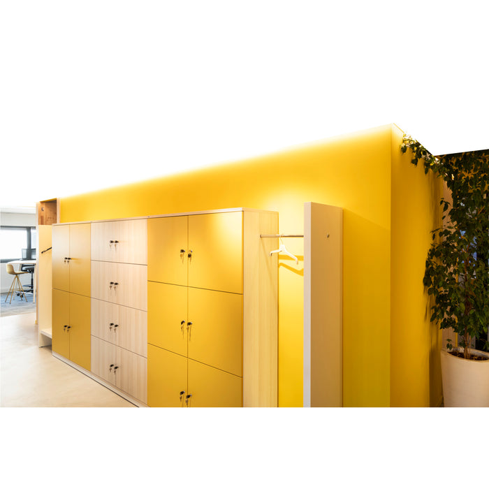 Built-in wood lockers, yellow and light wood finish, with keys, next to a yellow wall and plant.