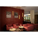 Gold cylinder pendant lights, suspended, in a red-walled lounge with red fabric armchairs and round tables.