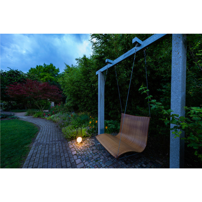 Wicker swing chair with metal frame, suspended in a garden setting.