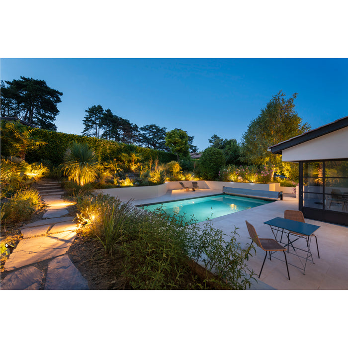 Backyard pool with stone patio, landscape lighting, and blue metal bistro table.