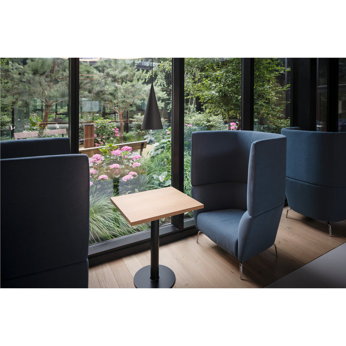 Upholstered blue privacy chair with wood table and black metal base.