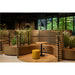 Modern office lounge area with curved wood benches, round table, yellow ottoman, and black pendant light.