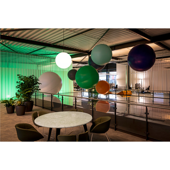 Modern office interior with hanging colorful spheres, round marble table, and olive green chairs.