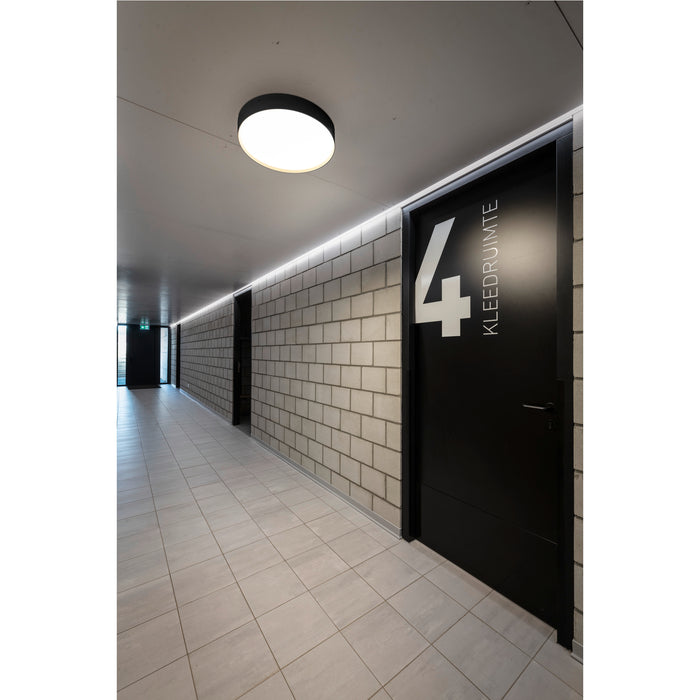 Hallway with black doors, concrete block walls, tile floors, and a round, ceiling-mounted light fixture.
