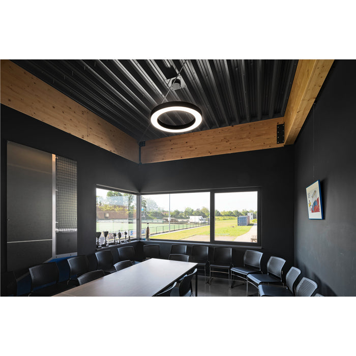 Black ring LED pendant light fixture, suspended from a black metal ceiling in a meeting room.