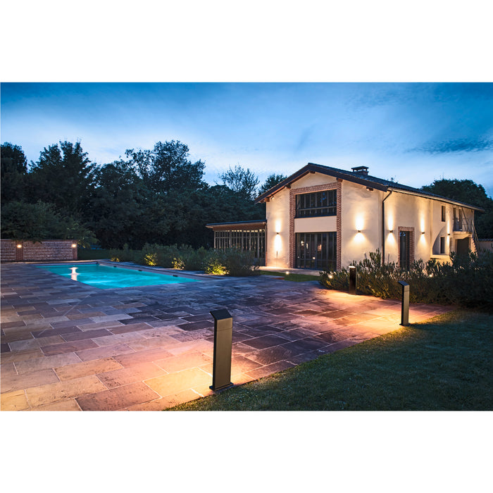 Black bollard lights illuminate a stone patio and pool area at dusk.