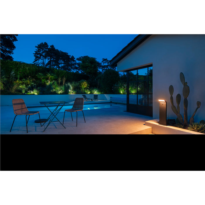 Black metal outdoor path light fixture, surface mounted, illuminating a modern patio at night.