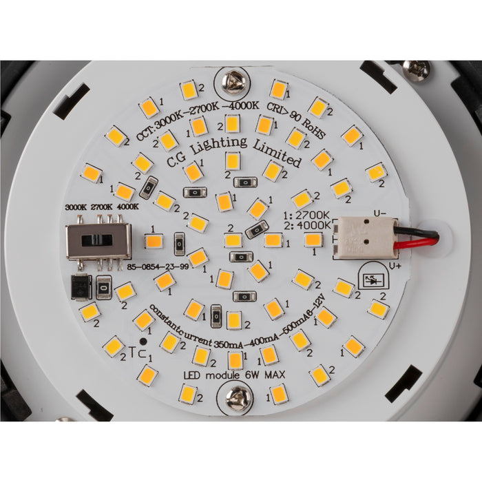 Close-up of a round, white LED module with yellow LEDs, various electronic components, and black and red wires.