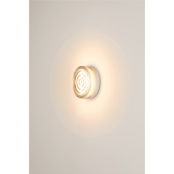 Clear glass wall sconce with a white base, mounted on a white wall.
