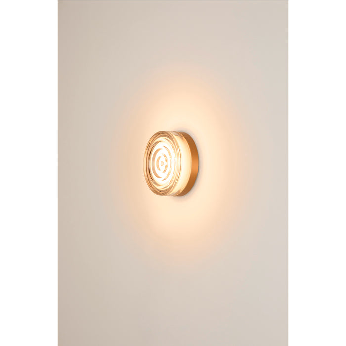 Clear glass wall sconce with concentric circle design and gold-tone metal mounting.