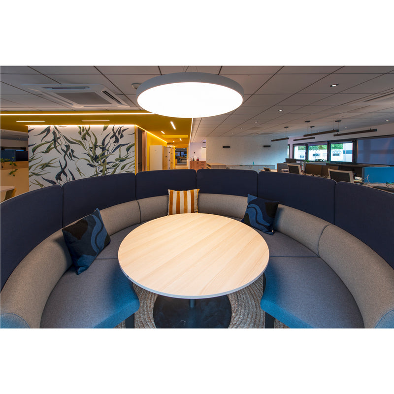 Office booth with blue fabric panels, light wood table, and gray upholstered seating.