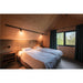 Bedroom with wood paneling, white linens, black track lighting, and dark green curtains.