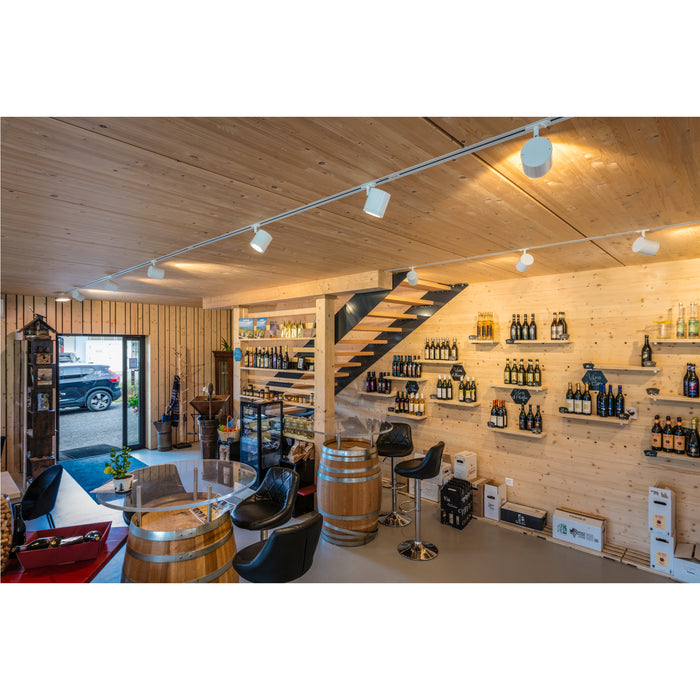 Wine shop interior with wood walls, barrel tables with glass tops, black leather chairs, and shelves of wine bottles.