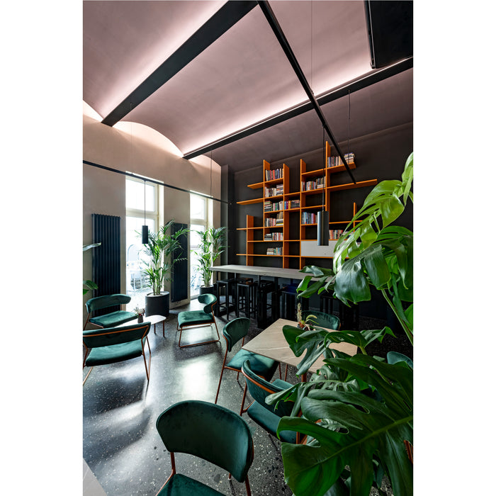 Interior of a cafe with green velvet chairs, terrazzo floor, orange bookshelf, and large Monstera plant.