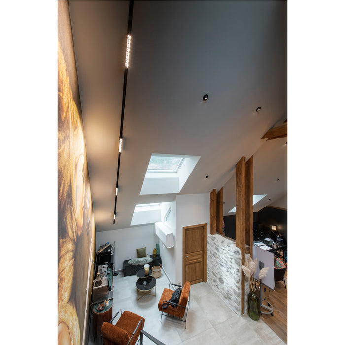 Interior view of a modern loft with skylights, track lighting, stone wall, and orange armchairs.