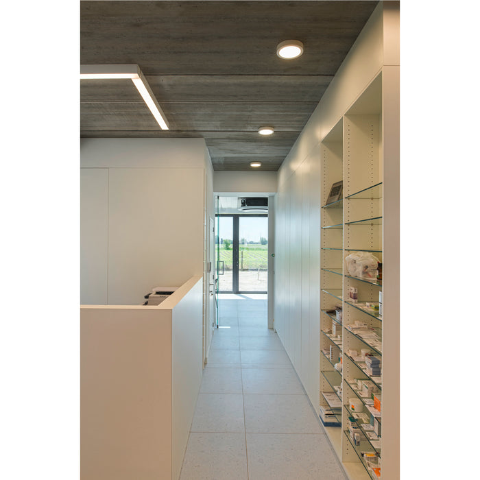 Modern hallway with concrete ceiling, flush-mount lighting, white cabinets, glass shelves, and light gray terrazzo tile flooring.