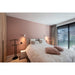 Bedroom with white floral-patterned quilt, pink pillows, black metal valet stand, and wall-mounted white sconces.