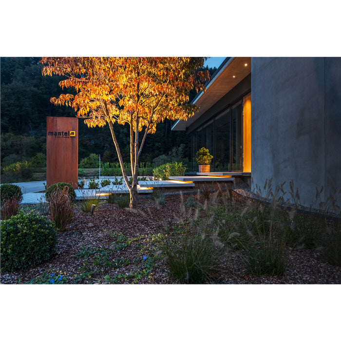 Exterior view of modern building with rusted metal sign and landscaping.