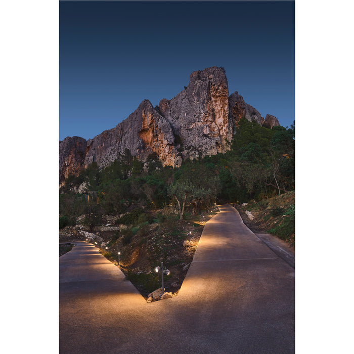 Illuminated stone path leading to rocky mountain at dusk.