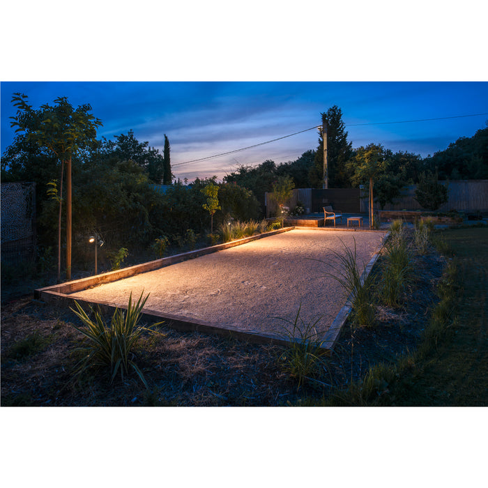 Outdoor bocce ball court with wood frame and gravel fill, illuminated at dusk.