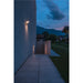 Modern gray wall-mounted LED light fixture illuminating a walkway at dusk.